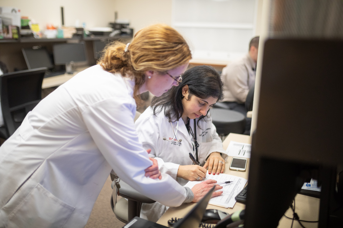 image of two diverse women in white lab coats looking over paperwork at medical office desk