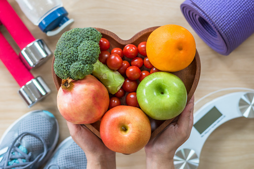 heart shaped bowl of fruit surrounded by workout tools