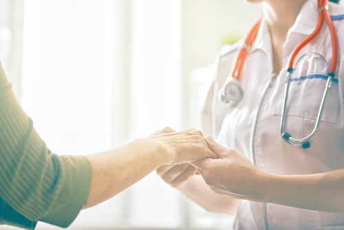 medical professional in white coat wearing stethoscope holding the hand of a patient