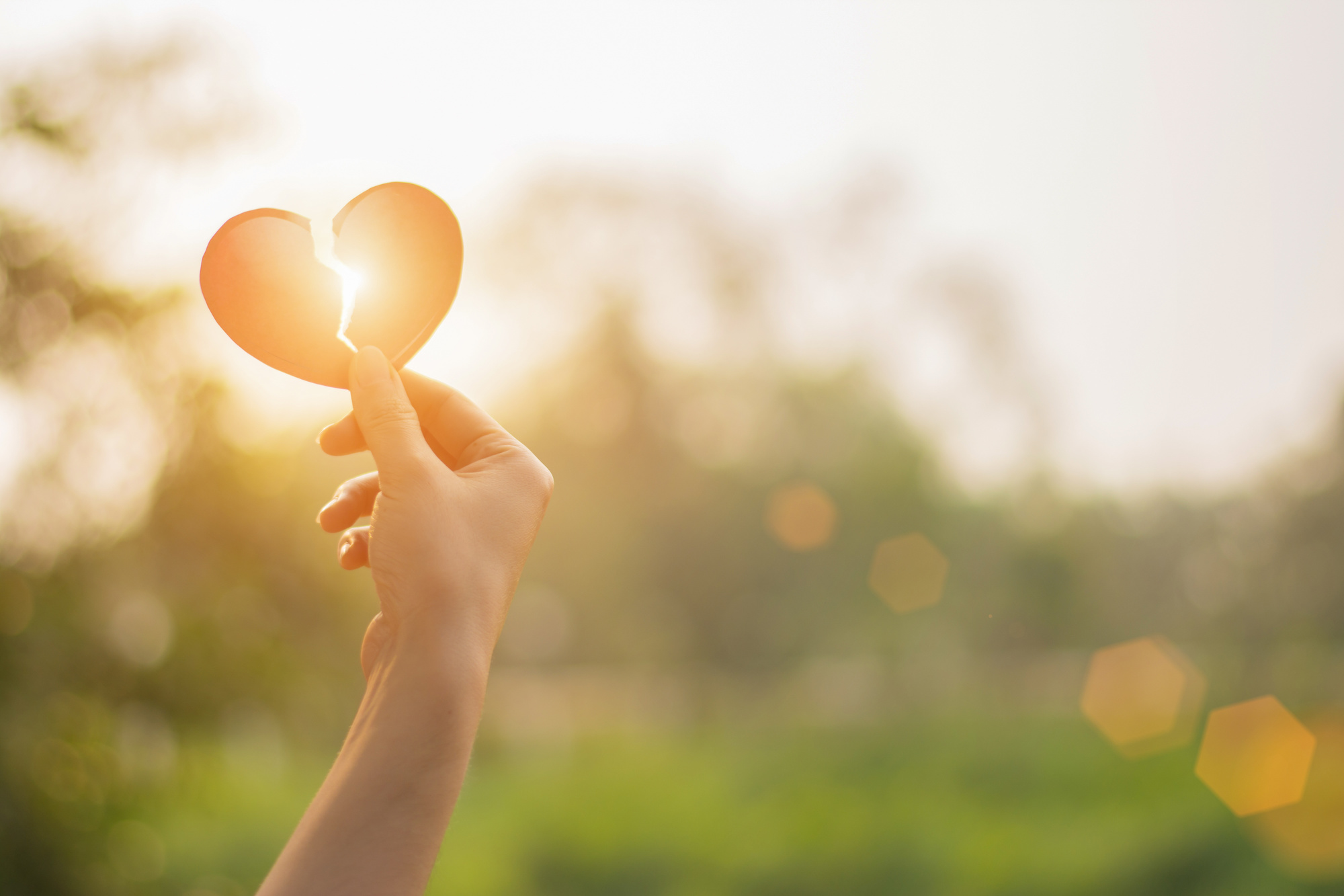 close up woman hand holding paper broken heart in the park