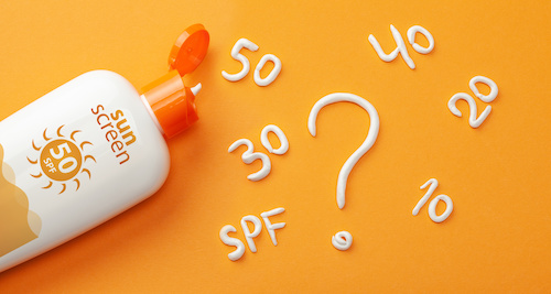 Sunscreen on orange background. Plastic bottle of sun protection and white cream in the form of question mark and numbers SPF"