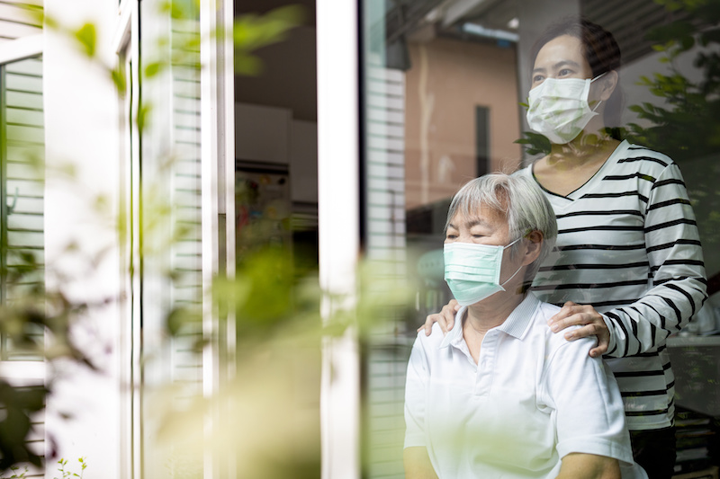 Caregiver woman is standing over the shoulder of sitting woman and both are looking out the window