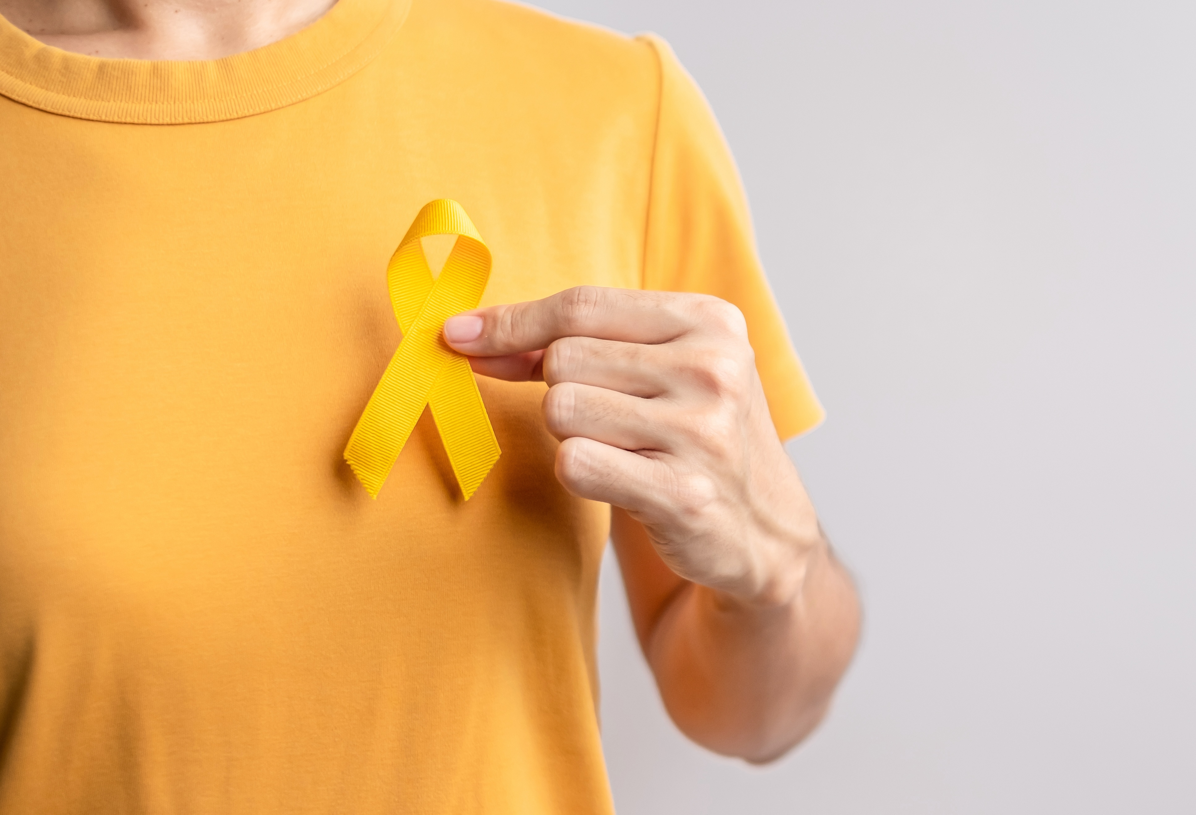 Woman in yellow t-shirt holding Sarcoma awareness ribbon against her chest