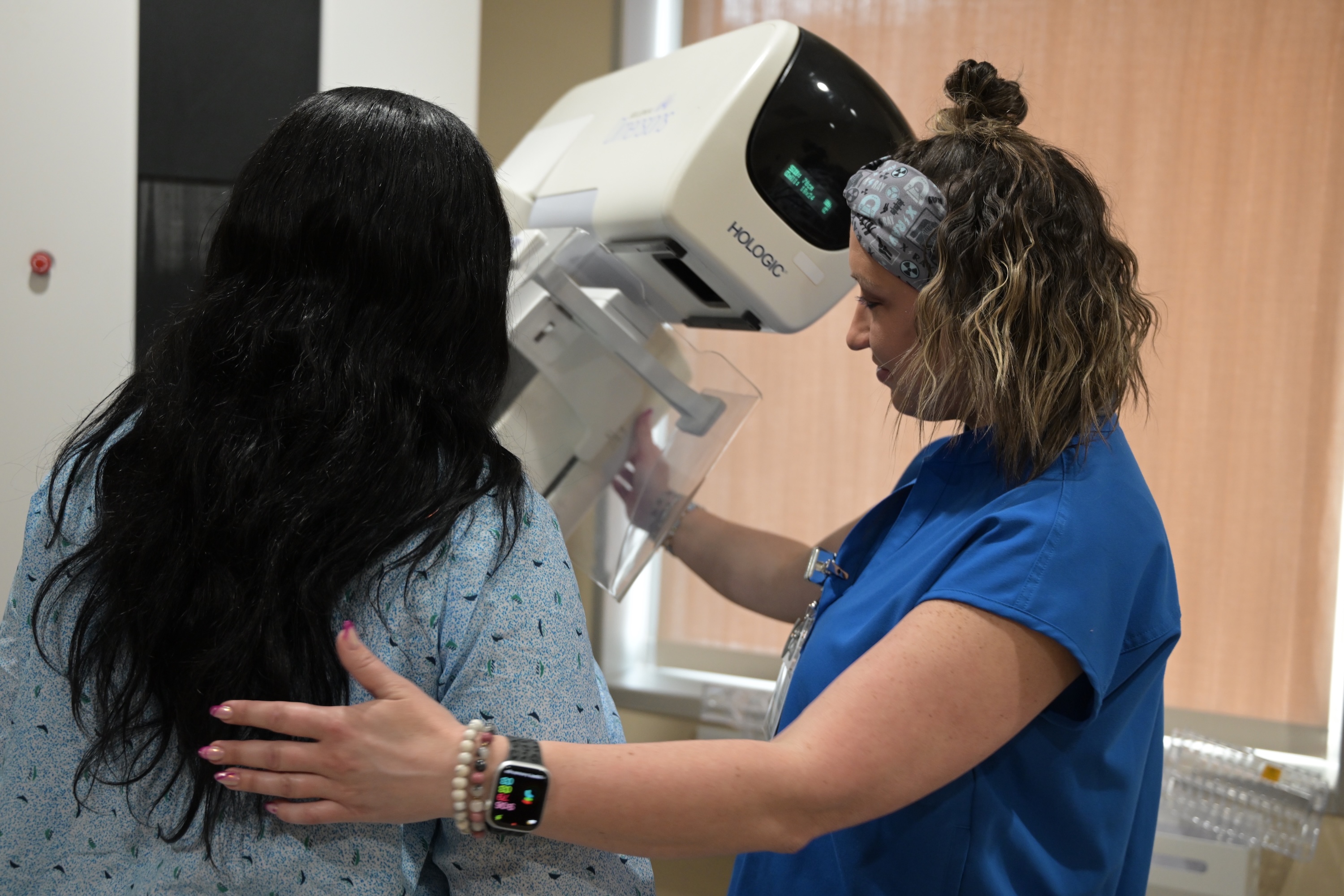 Woman in blue scrubs performing mammogram on patient in hospital gown