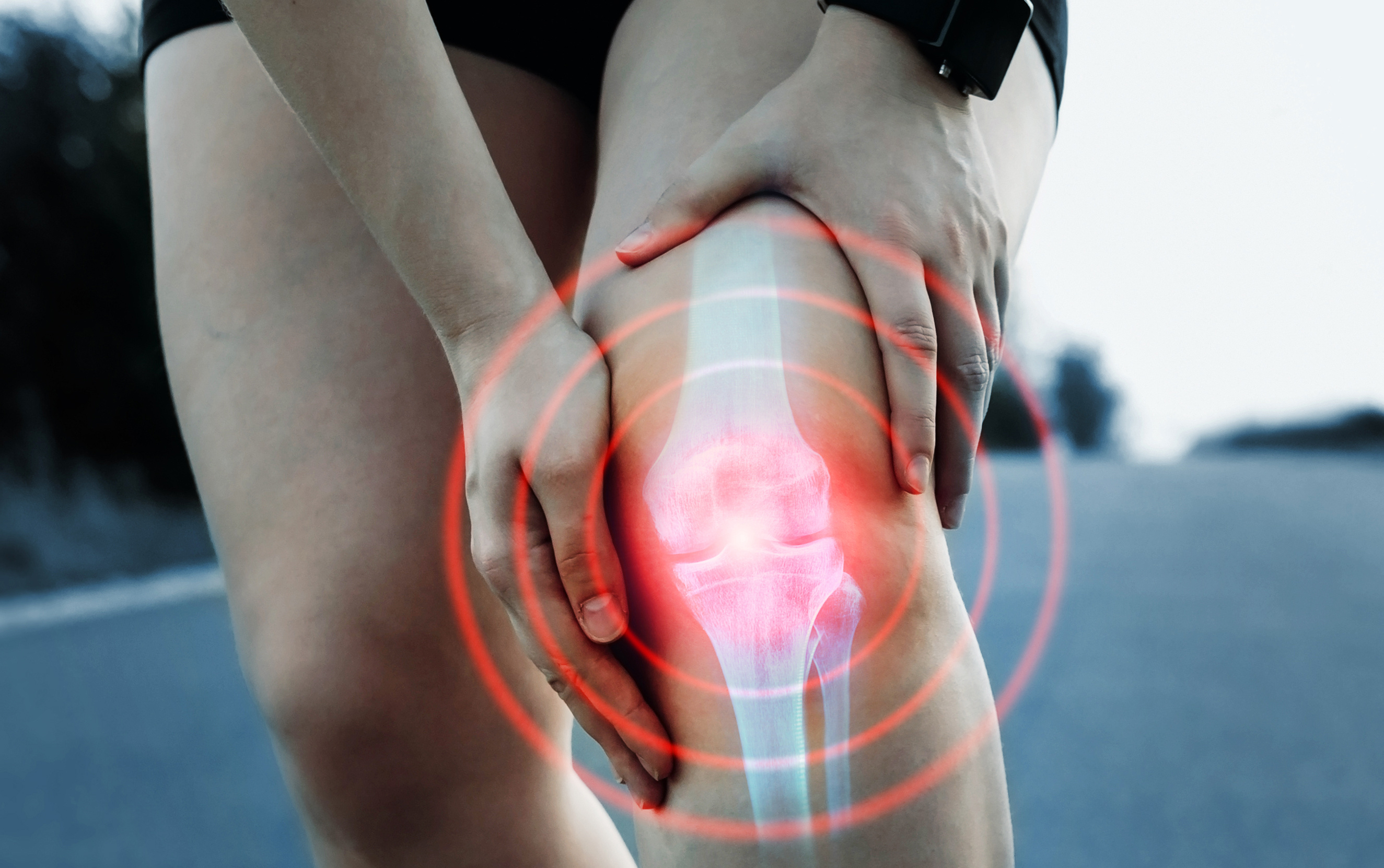 Close up of person grabbing arthritic knee joint in pain while running outdoors