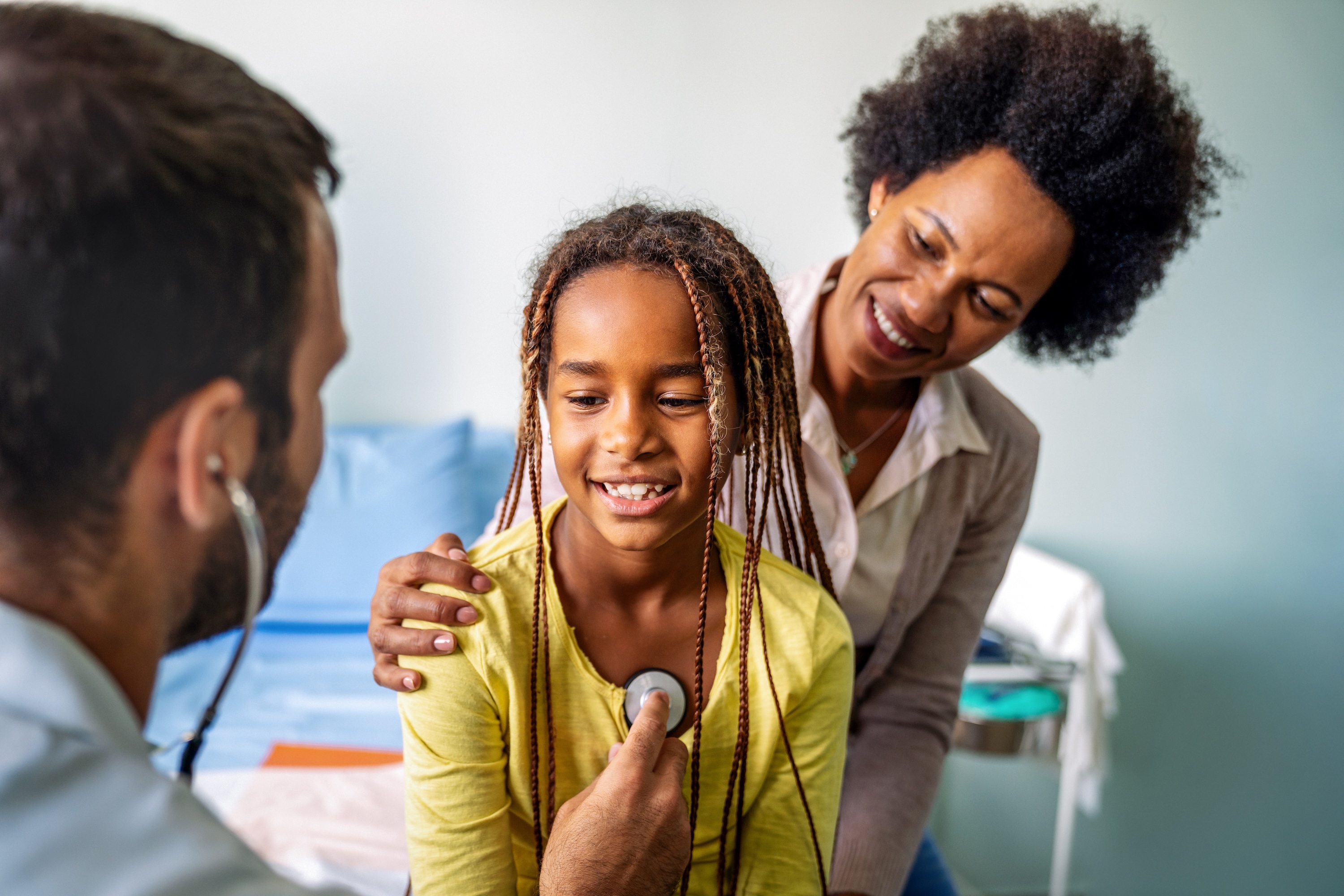 Young girl held by mother being examined by doctor using stethoscope