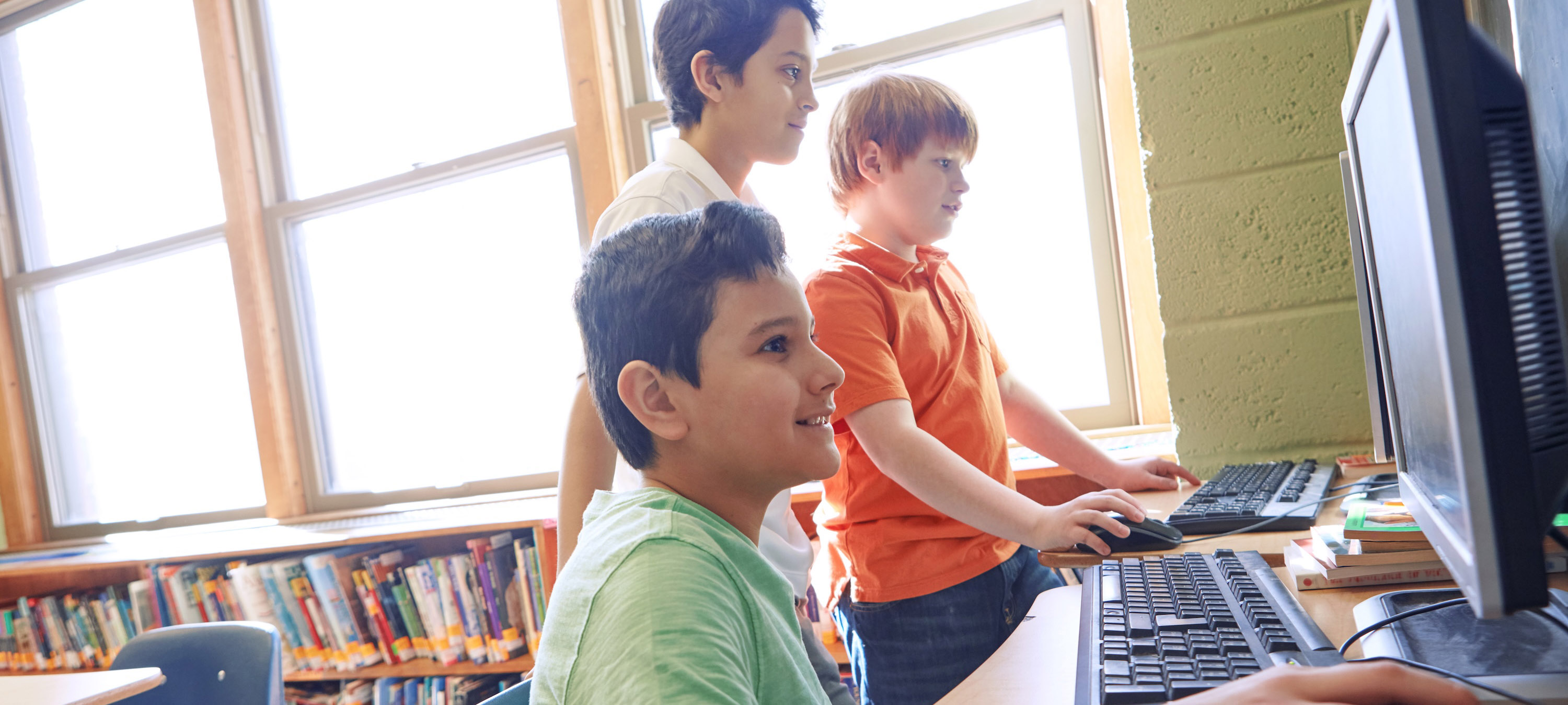 Three smiling, young boys using computers in classroom