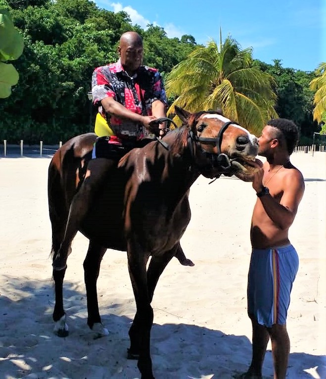 Dave Rodney rides a horse on a sandy beach.