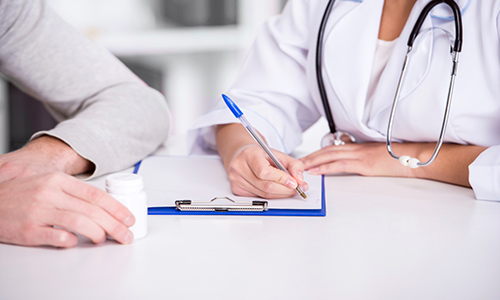 photo of doctor sitting at table writing on a clipboard across from patient