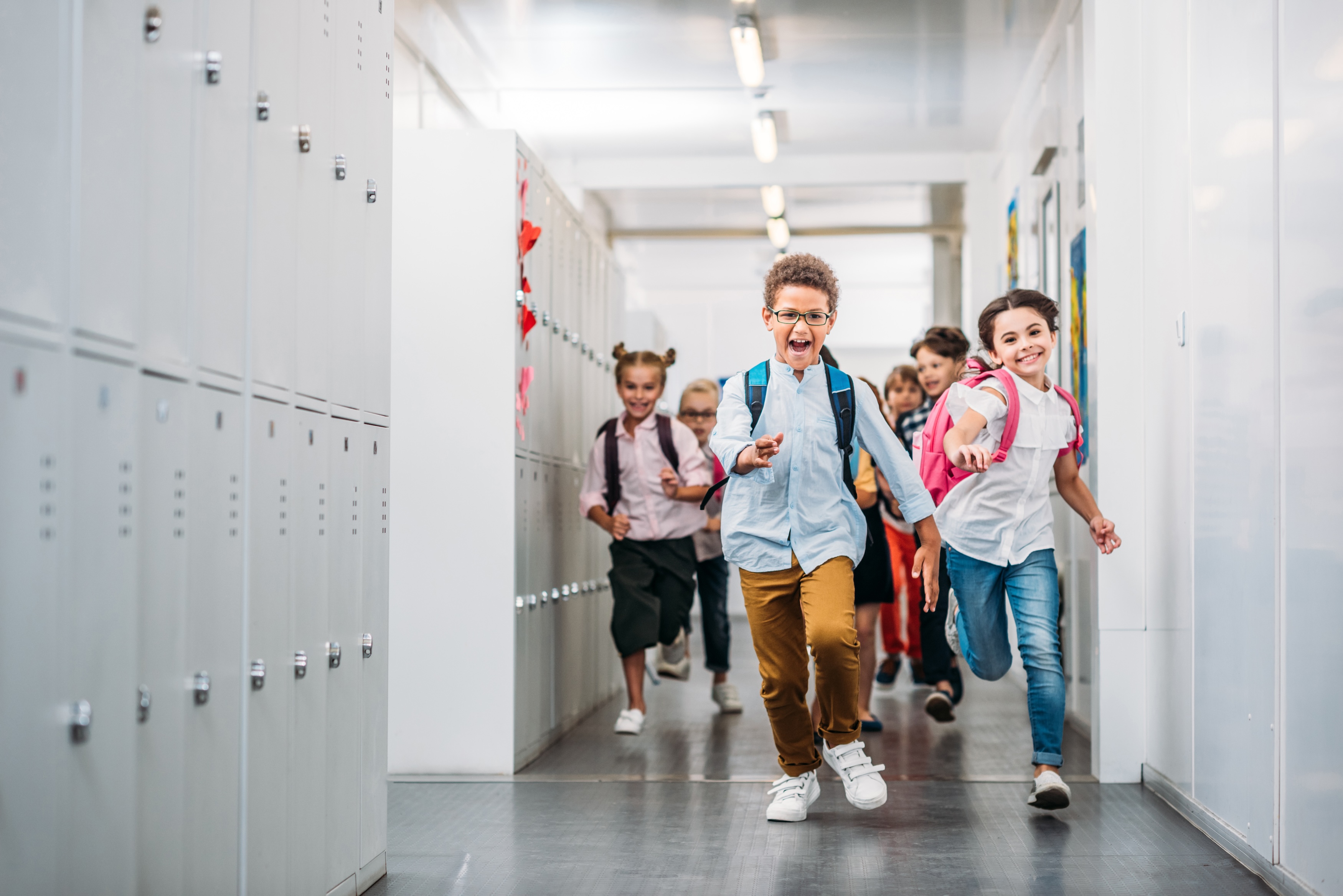 Children running down school hallway while smiling