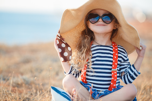 little girl sitting on a beach wearing sunglasses and a large sun hat