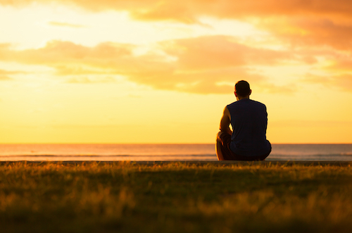 man sitting on a hill under a sunset 