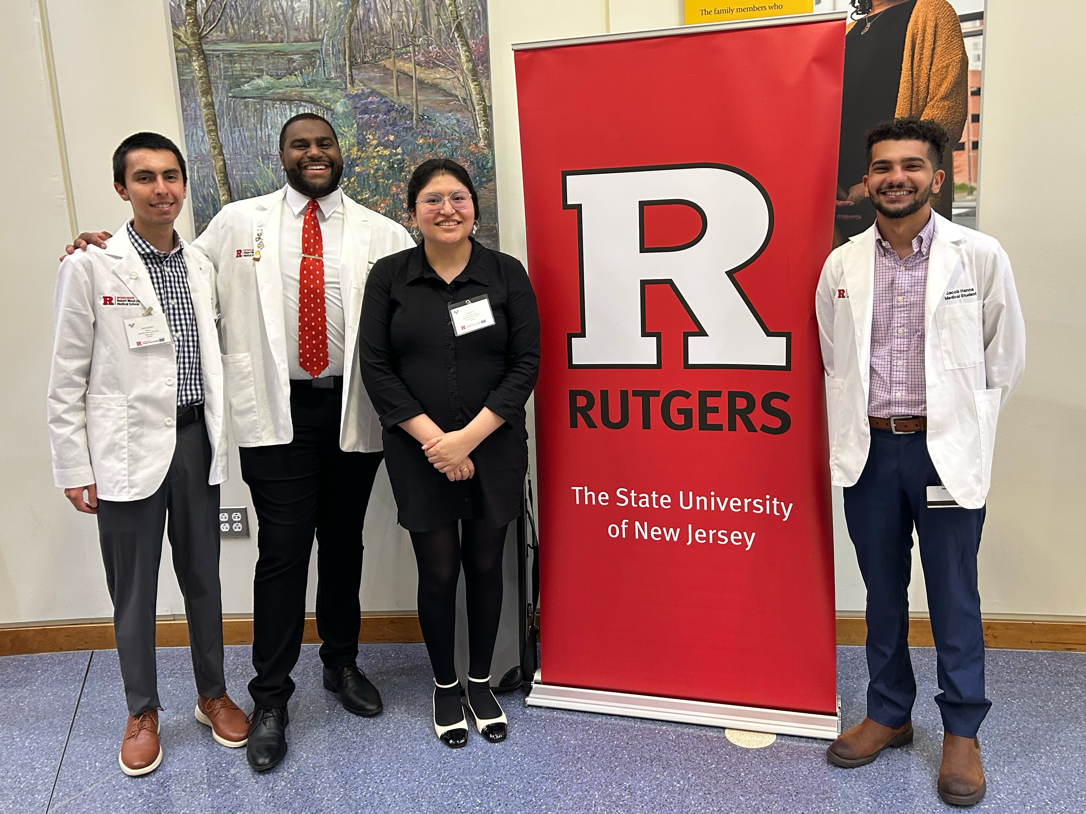 4 OPTIM group members standing in front of Rutgers Banner