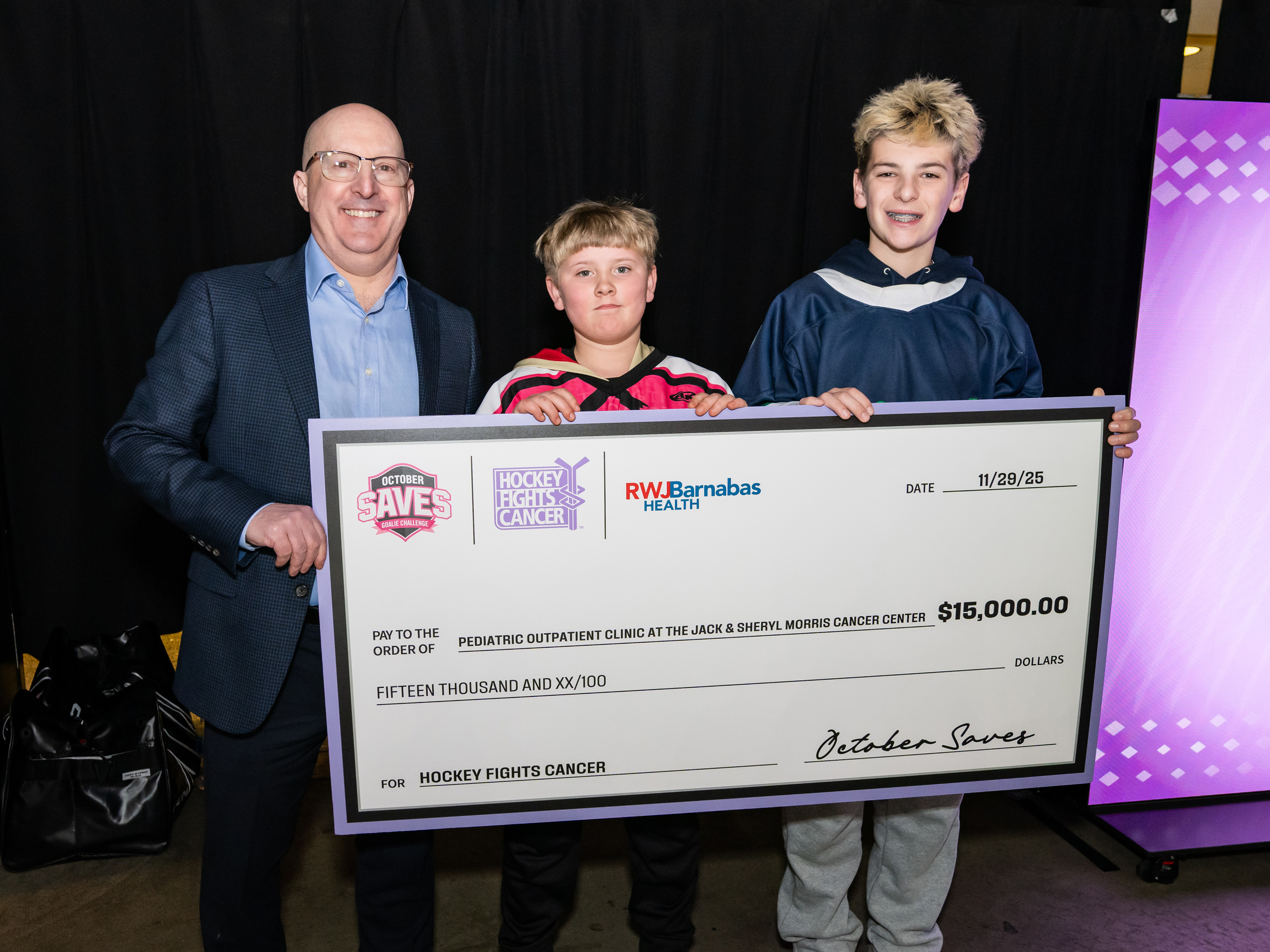 3 Individuals holding donation check at NJ Devils hockey game